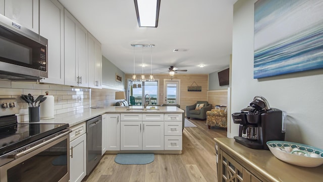 kitchen with a peninsula, a sink, visible vents, appliances with stainless steel finishes, and light wood-type flooring