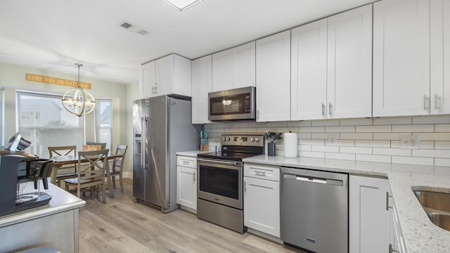 kitchen with stainless steel appliances, visible vents, white cabinets, light wood-style floors, and decorative backsplash