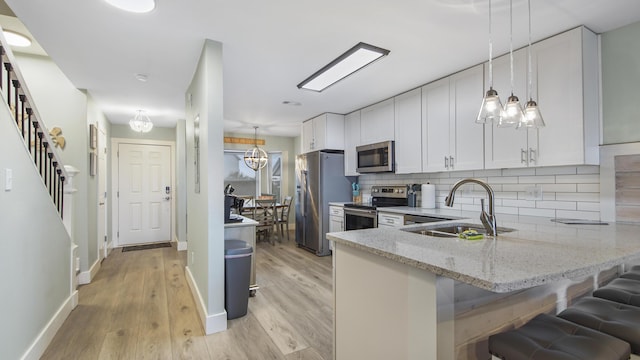 kitchen with tasteful backsplash, appliances with stainless steel finishes, white cabinetry, a sink, and light stone countertops