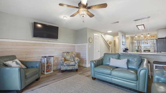 living area featuring stairway, wood finished floors, visible vents, and a ceiling fan