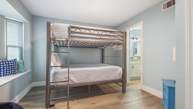 bedroom featuring visible vents, connected bathroom, baseboards, and wood finished floors