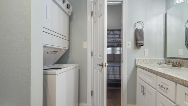 laundry area featuring stacked washer and dryer, laundry area, a sink, and wood finished floors