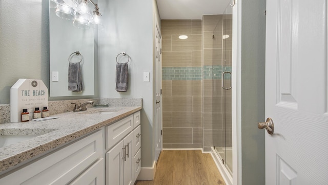 bathroom featuring a stall shower, wood finished floors, a sink, and double vanity