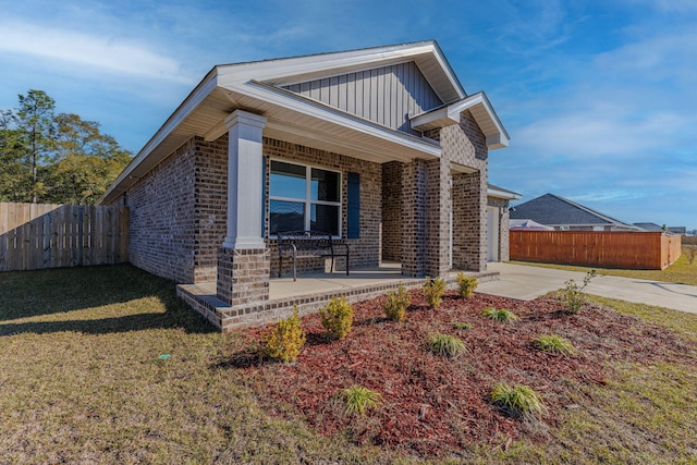 view of front of house featuring brick siding, covered porch, board and batten siding, fence, and a front lawn