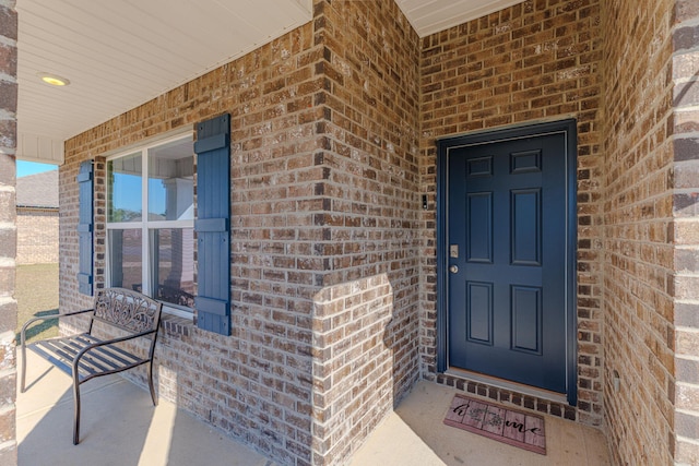 view of exterior entry featuring brick siding and a porch