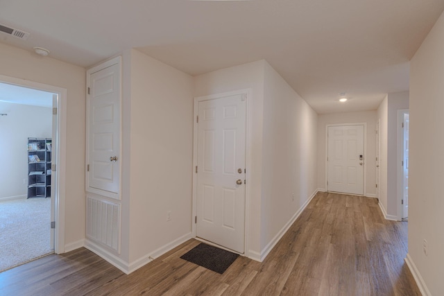 hallway with baseboards, visible vents, and wood finished floors