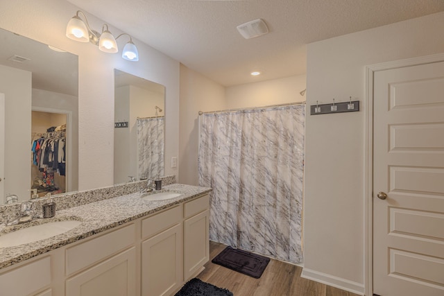 bathroom featuring a textured ceiling, double vanity, wood finished floors, and a sink