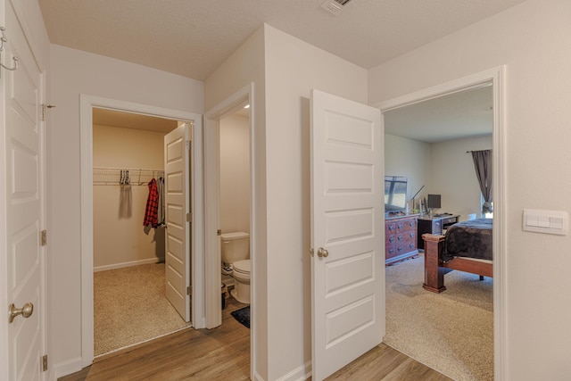 hall featuring a textured ceiling, light carpet, light wood-style flooring, and baseboards