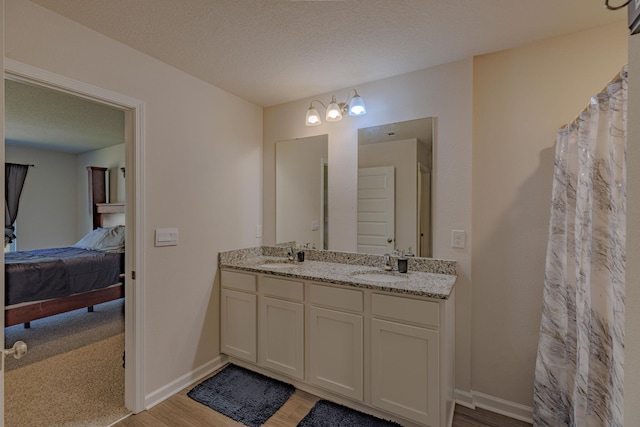 ensuite bathroom with a textured ceiling, double vanity, ensuite bath, and a sink