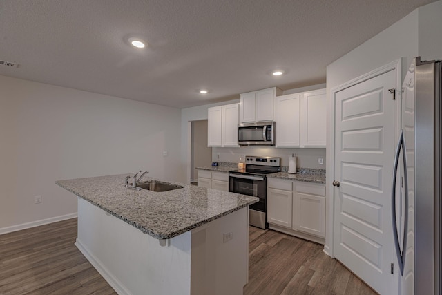 kitchen featuring white cabinets, an island with sink, dark wood-type flooring, stainless steel appliances, and a sink