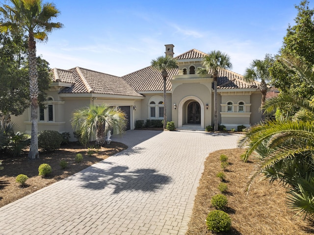 mediterranean / spanish-style house with a garage, decorative driveway, a tiled roof, and stucco siding