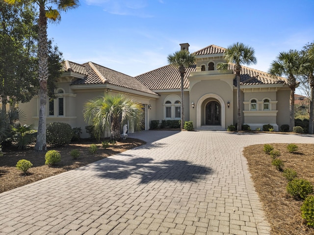 mediterranean / spanish-style home with a garage, decorative driveway, a tile roof, and stucco siding