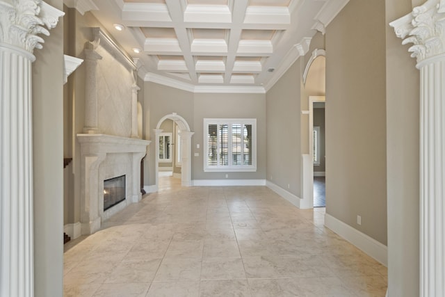 unfurnished living room featuring arched walkways, coffered ceiling, a premium fireplace, ornate columns, and beam ceiling