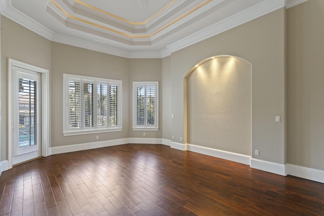 spare room with arched walkways, a raised ceiling, and wood finished floors