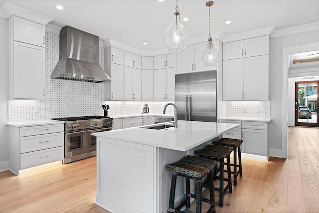 kitchen with light wood finished floors, high end appliances, light countertops, a sink, and wall chimney range hood