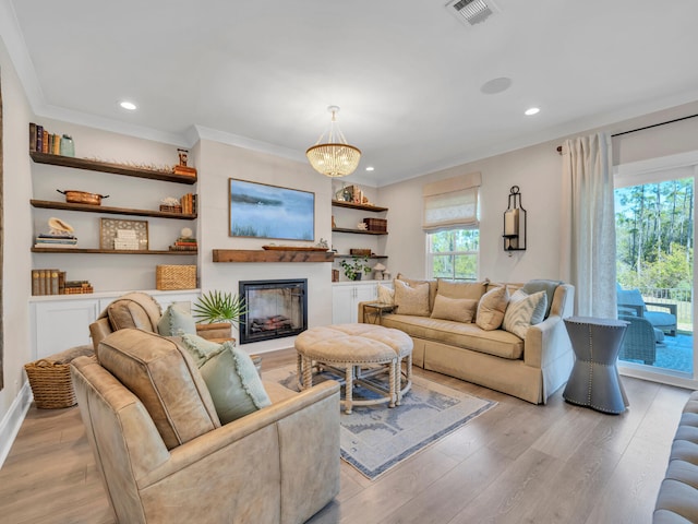 living room featuring visible vents, a glass covered fireplace, light wood-style flooring, ornamental molding, and a notable chandelier