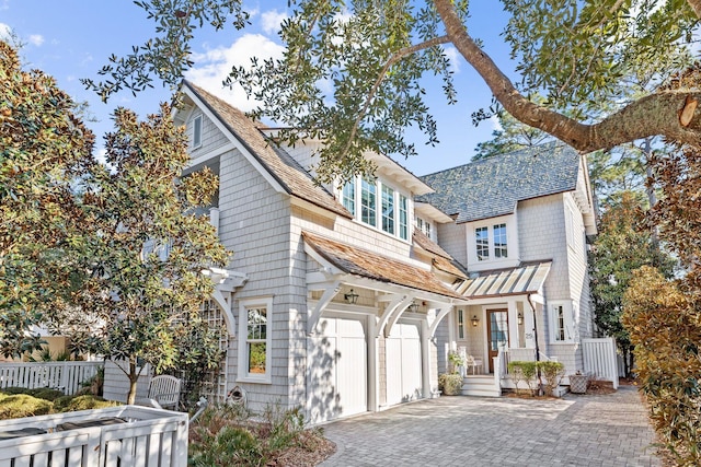 shingle-style home with a garage, decorative driveway, and fence