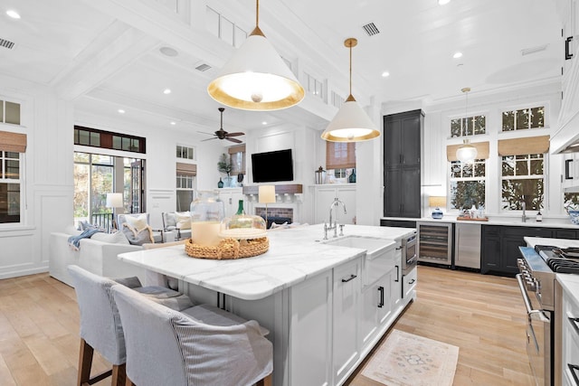 kitchen with beverage cooler, open floor plan, high end stainless steel range, a decorative wall, and a sink