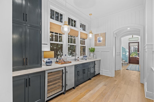 bar featuring arched walkways, wine cooler, a decorative wall, a sink, and light wood-style floors