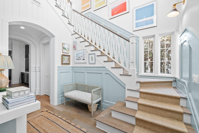 stairway featuring a high ceiling, arched walkways, a decorative wall, and wood finished floors