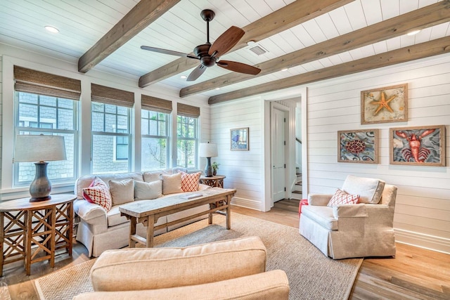 living area with ceiling fan, baseboards, stairway, light wood finished floors, and beamed ceiling
