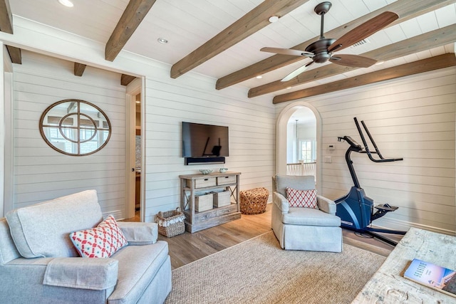 living room featuring arched walkways, a ceiling fan, wood walls, wood finished floors, and beamed ceiling