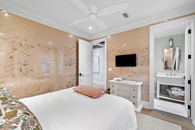 bedroom featuring wood finished floors, visible vents, baseboards, ensuite bath, and wallpapered walls