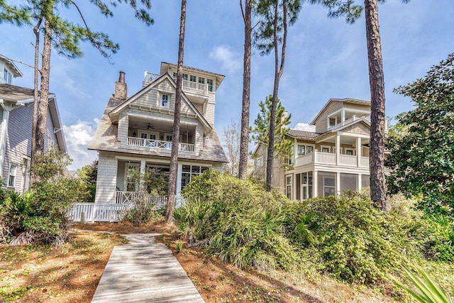 rear view of property with ceiling fan, a chimney, and a balcony