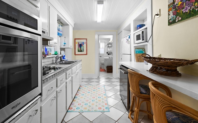 kitchen featuring stainless steel appliances, light countertops, white cabinets, a sink, and light tile patterned flooring