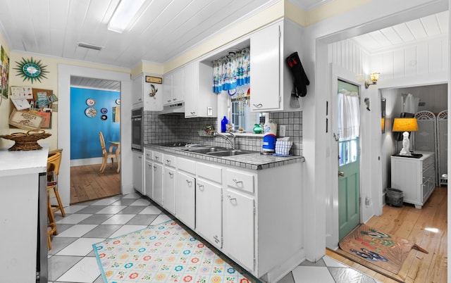 kitchen with visible vents, oven, under cabinet range hood, white cabinetry, and a sink