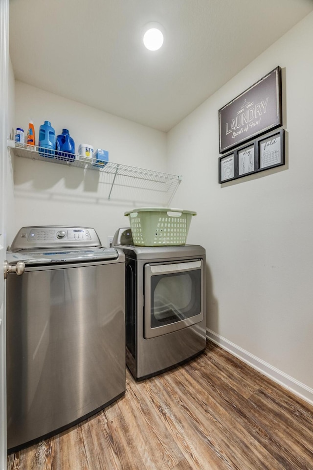 clothes washing area with washer and clothes dryer, laundry area, baseboards, and wood finished floors