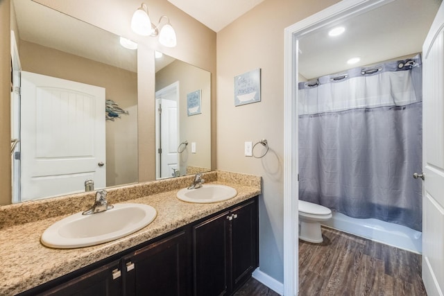 full bath with double vanity, toilet, wood finished floors, and a sink