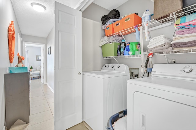 clothes washing area with light tile patterned flooring, laundry area, washer and dryer, and a textured ceiling