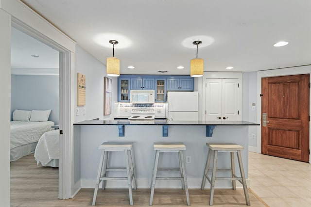 kitchen with dark countertops, blue cabinetry, a kitchen breakfast bar, a peninsula, and white appliances