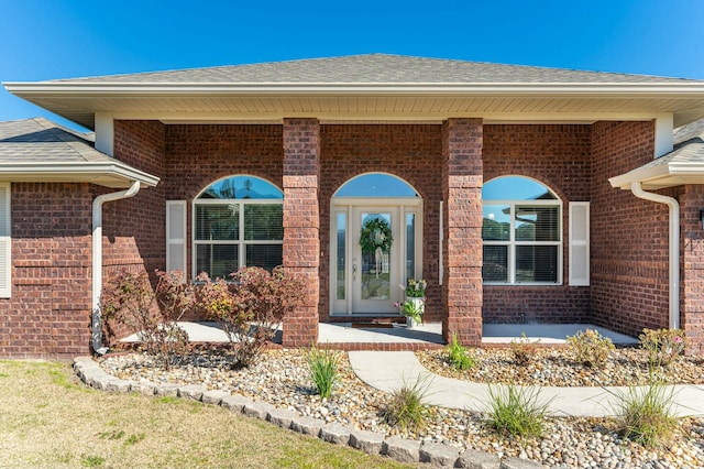 entrance to property featuring a shingled roof and brick siding