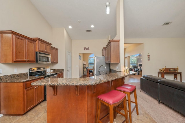 kitchen with a peninsula, appliances with stainless steel finishes, a breakfast bar, and visible vents