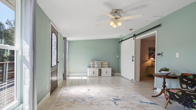 interior space with a barn door, visible vents, ceiling fan, and tile patterned floors