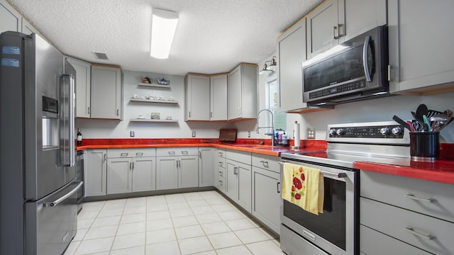 kitchen with a textured ceiling, gray cabinetry, stainless steel appliances, a sink, and visible vents