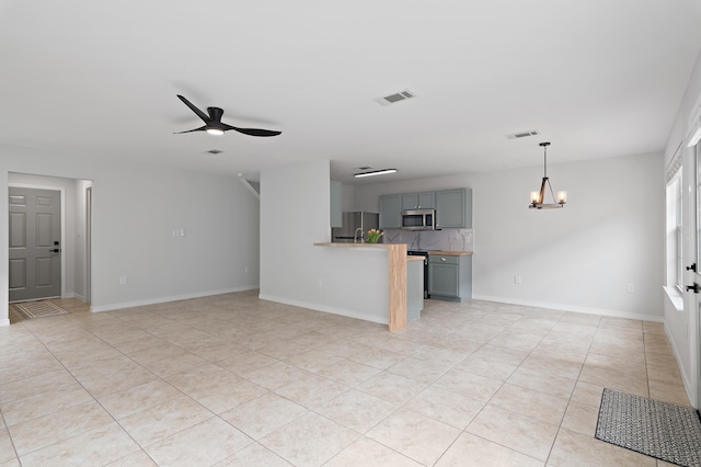 unfurnished living room with visible vents, baseboards, and ceiling fan with notable chandelier