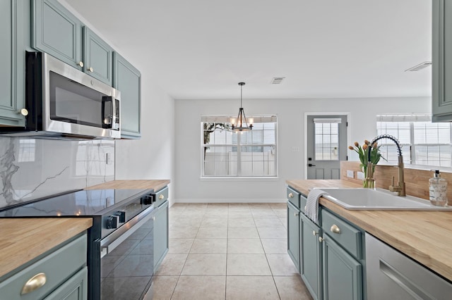 kitchen featuring stainless steel microwave, range with electric stovetop, wood counters, and a sink