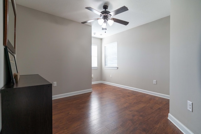 empty room featuring a ceiling fan, dark wood finished floors, and baseboards