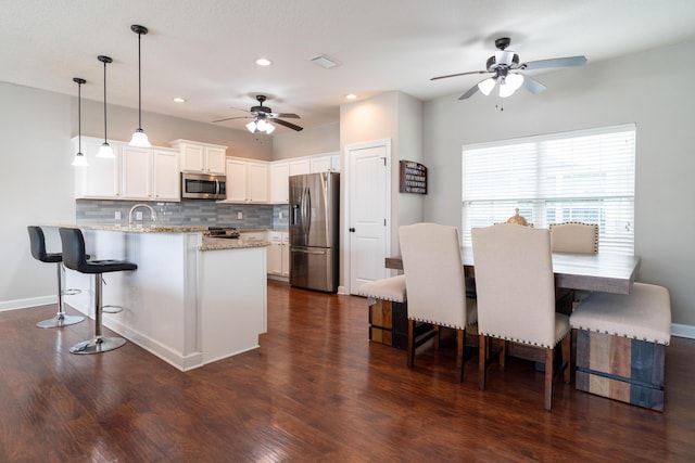 kitchen with a breakfast bar, dark wood-style flooring, backsplash, appliances with stainless steel finishes, and a peninsula