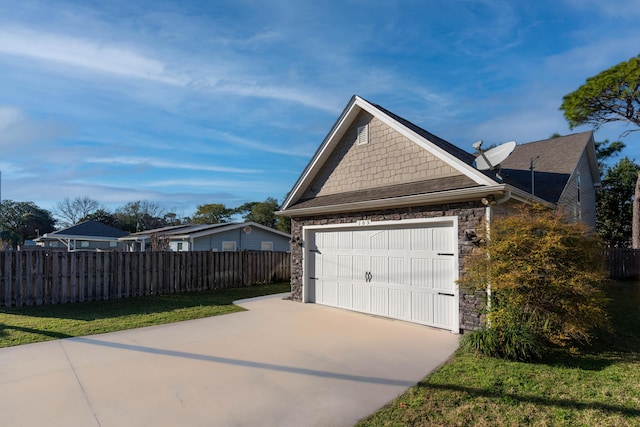 view of side of home featuring a garage, stone siding, fence, and driveway