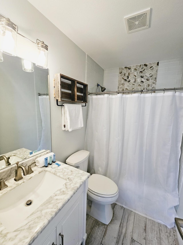 bathroom featuring curtained shower, toilet, wood finished floors, vanity, and visible vents