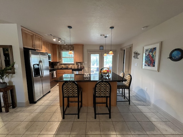 kitchen with light tile patterned floors, a breakfast bar area, stainless steel appliances, a sink, and dark countertops