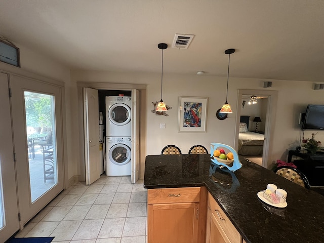 kitchen with light tile patterned floors, visible vents, dark stone counters, stacked washer / dryer, and decorative light fixtures