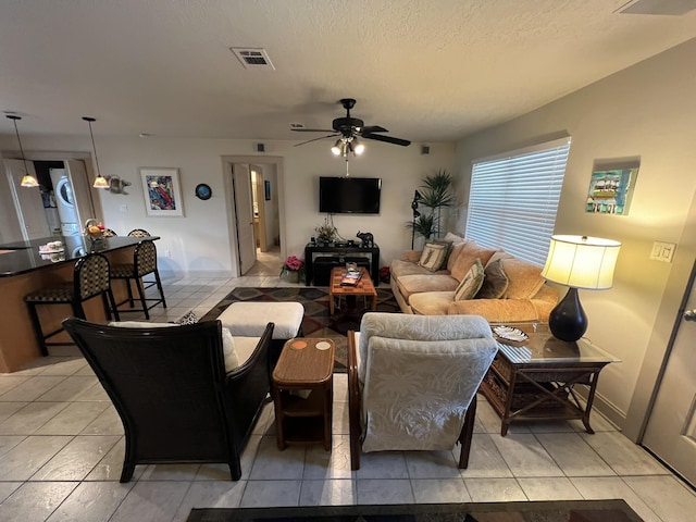 living area featuring ceiling fan, light tile patterned floors, a textured ceiling, and visible vents