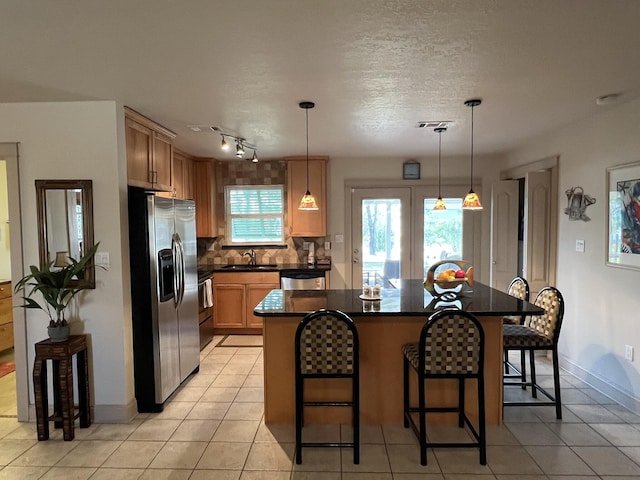 kitchen with stainless steel fridge, dark countertops, a breakfast bar area, a center island, and a sink