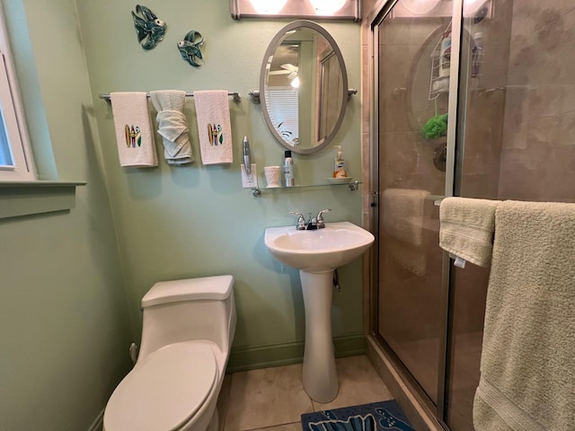 bathroom featuring toilet, a shower stall, baseboards, and tile patterned floors