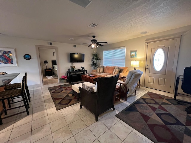 living area featuring light tile patterned floors, a ceiling fan, visible vents, and a textured ceiling